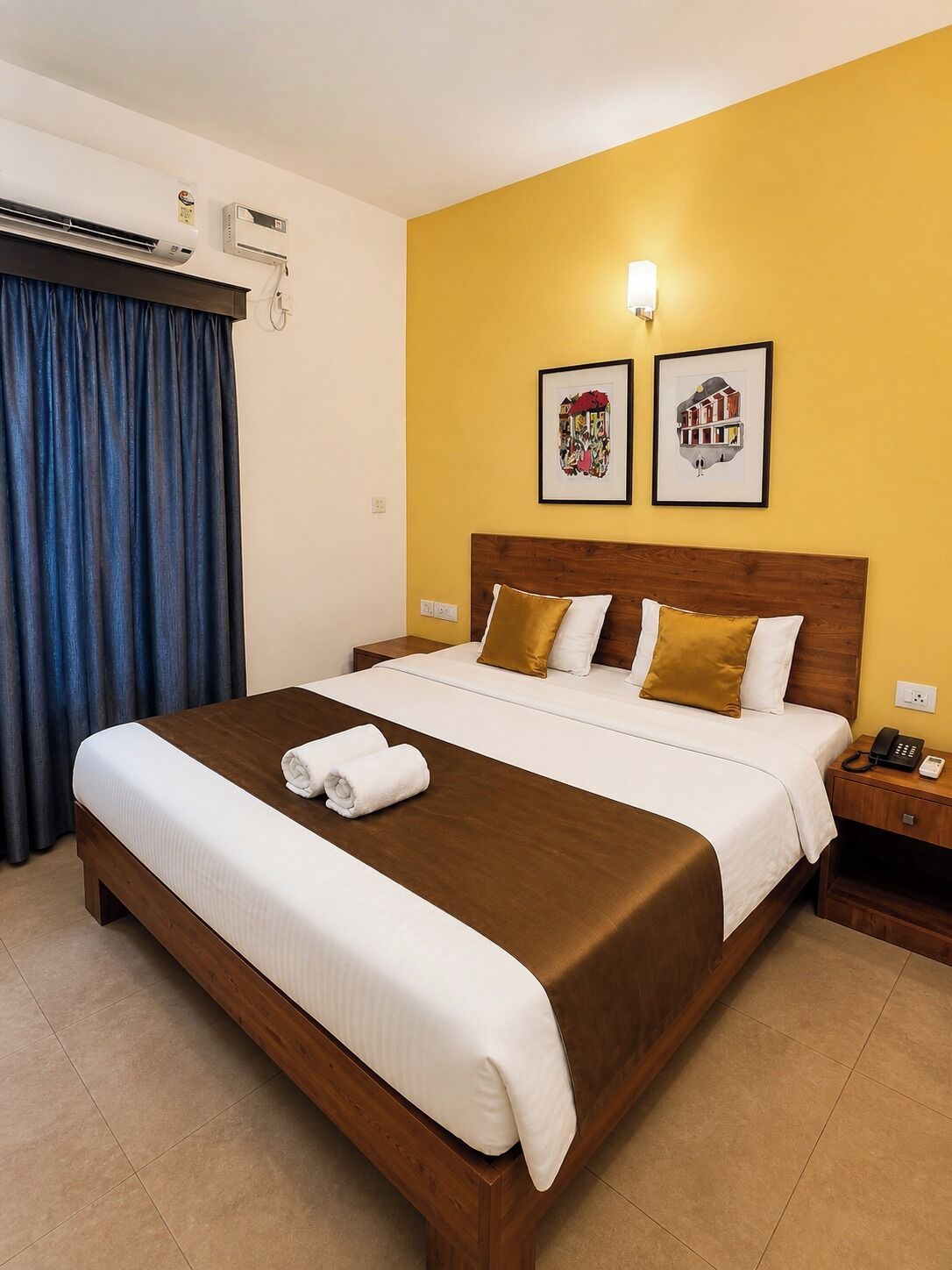 A hotel room with a large bed, a bedside table with a phone, and two framed pictures on the wall.