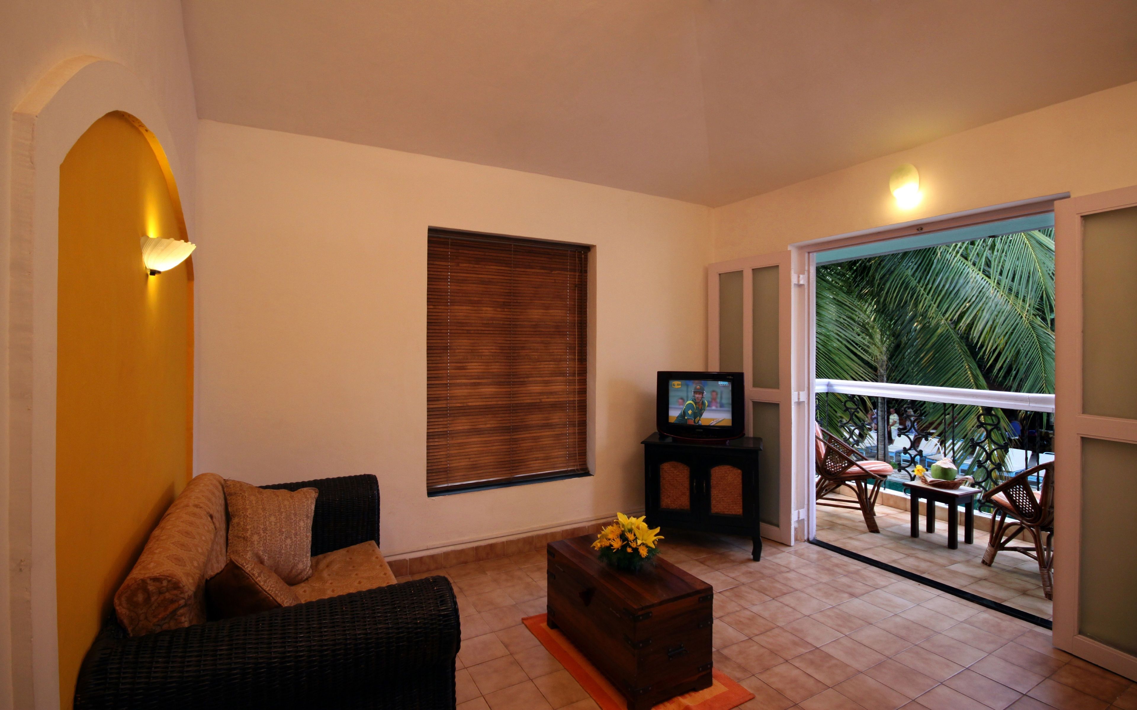 Una sala de estar con un sofá, una mesita con un florero, un televisor y una ventana con persianas.