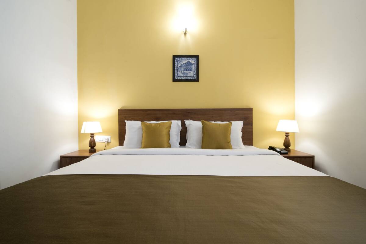 Una habitación de hotel con una cama grande, dos mesitas de noche con lámparas, y un cuadro en la pared.