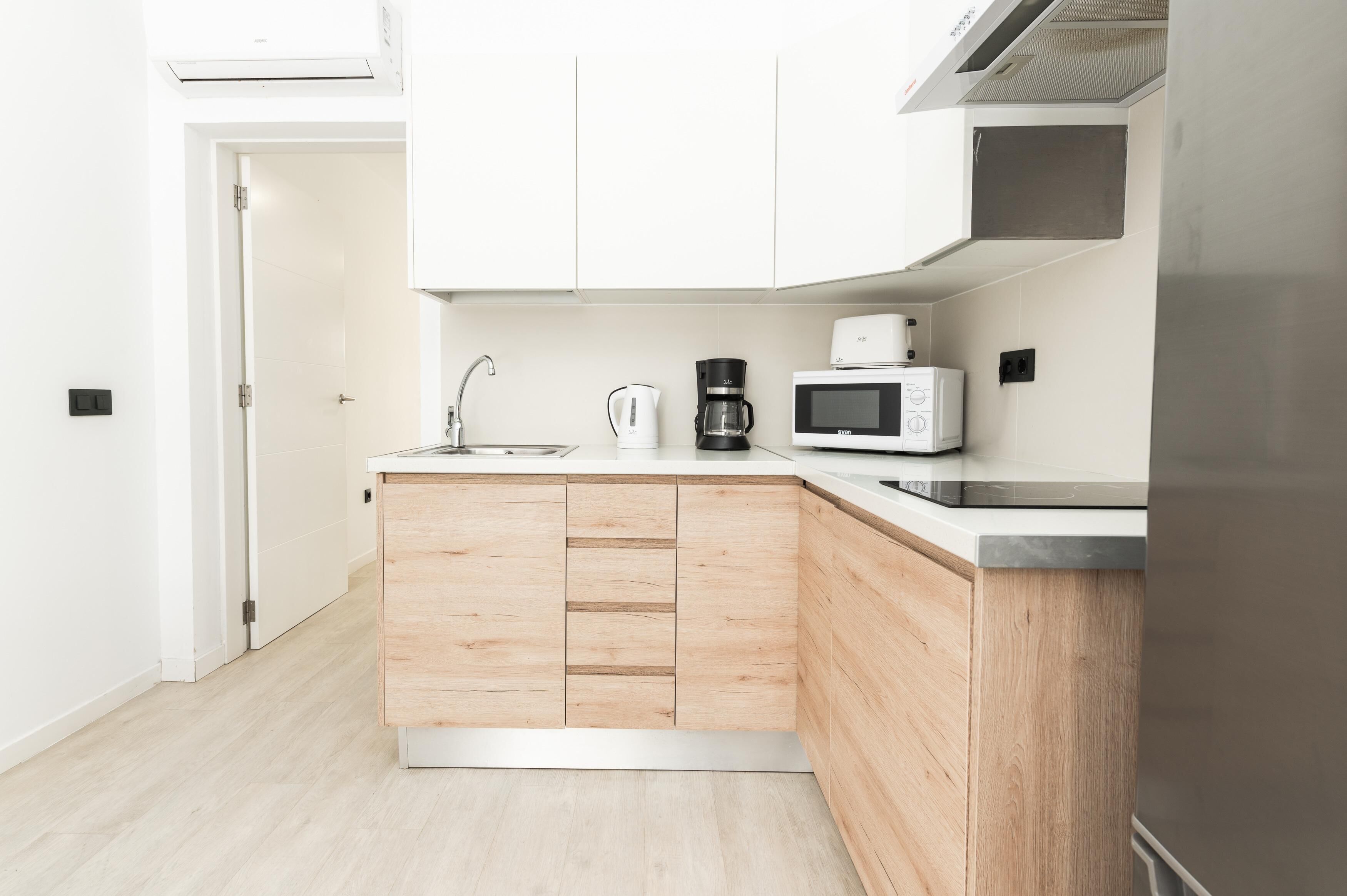Una cocina moderna con armarios blancos, un microondas, una cafetera y un lavabo.