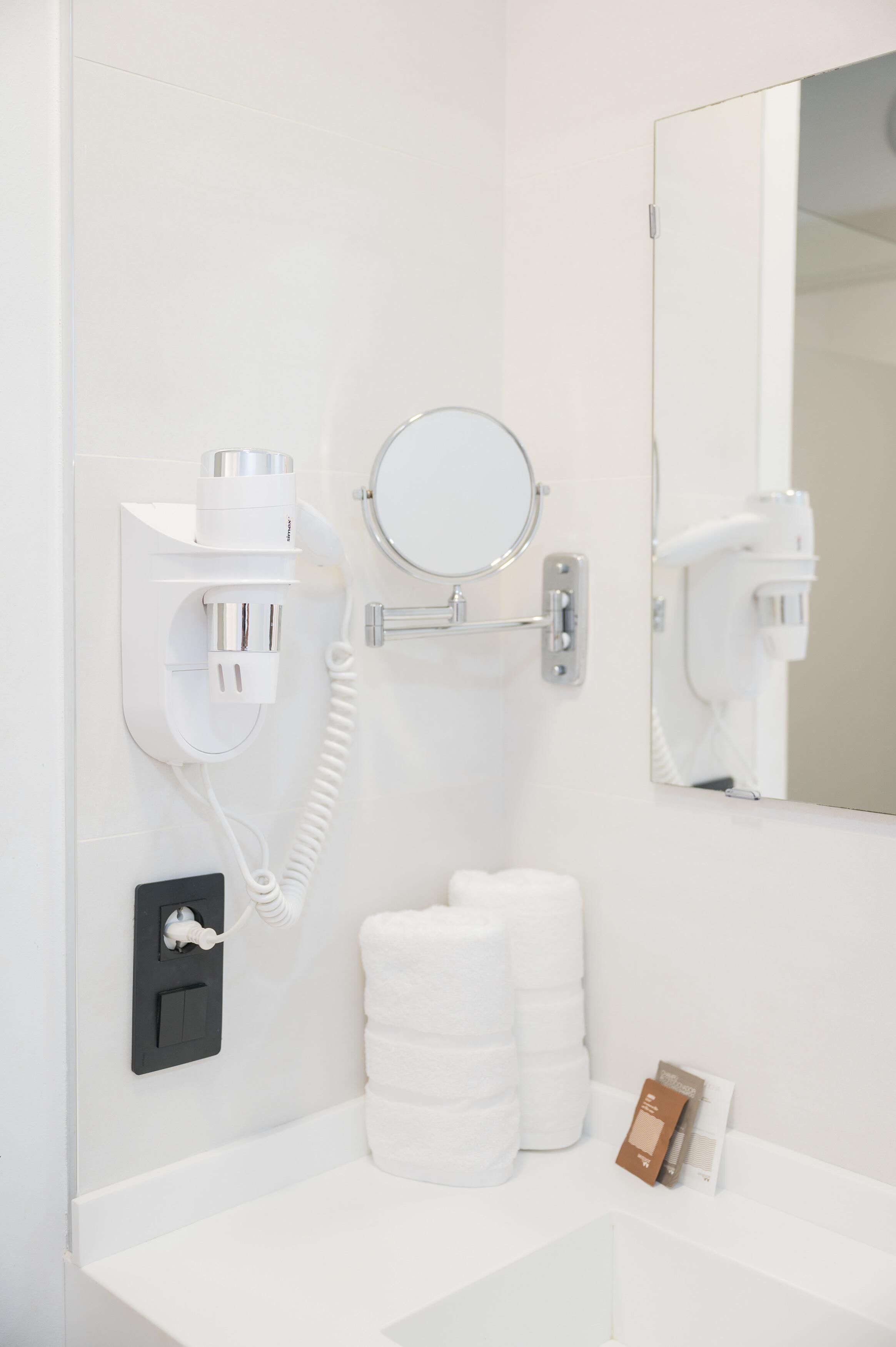 A bathroom with a white sink, a mirror, a hairdryer, and a towel dispenser.