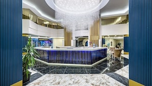 A modern lobby with a central reception desk, a chandelier, and a high ceiling. - Blue Star Hotel Alanya (Alanya)