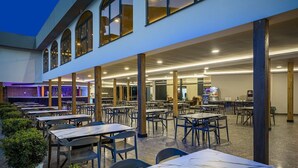 An outdoor dining area with tables and chairs, a covered section with a bar, and a building with large windows. - Blue Star Hotel Alanya (Alanya)