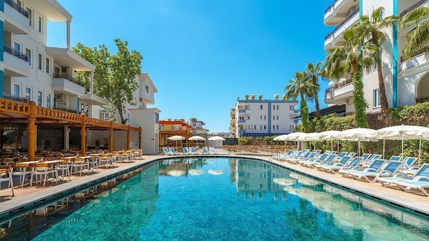 A swimming pool with lounge chairs and umbrellas, surrounded by buildings with balconies and palm trees. - Blue Star Hotel Alanya (Alanya)