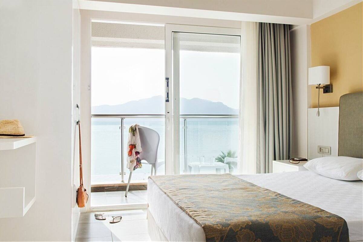 A hotel room with a bed, a chair, a table, and a view of the sea.