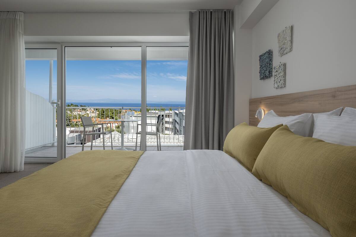 Ein Hotelzimmer mit einem großen Bett, einem Balkon mit Meerblick und einem Holzkopfende.
