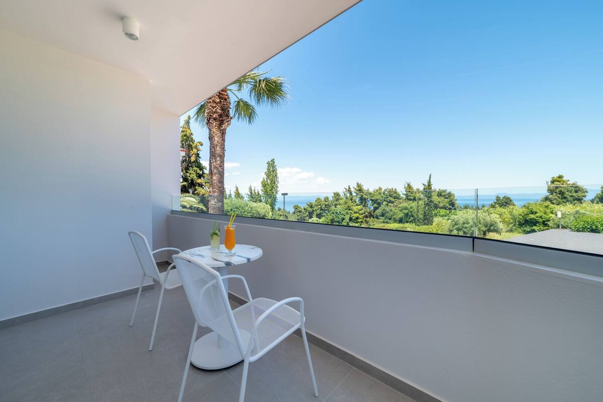 Ein Balkon mit Tisch und Stühlen, Blick aufs Meer und eine Palme.