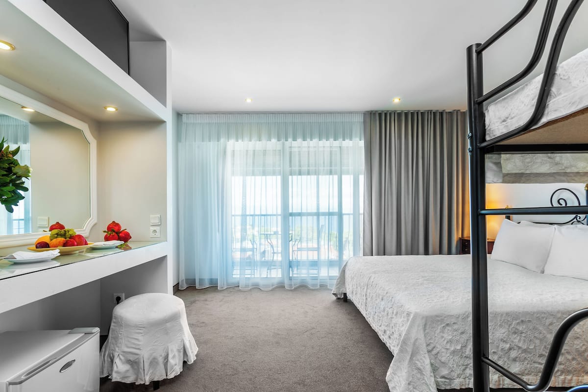 A hotel room with a bunk bed, a desk with a mirror, a small stool, and a window with curtains.