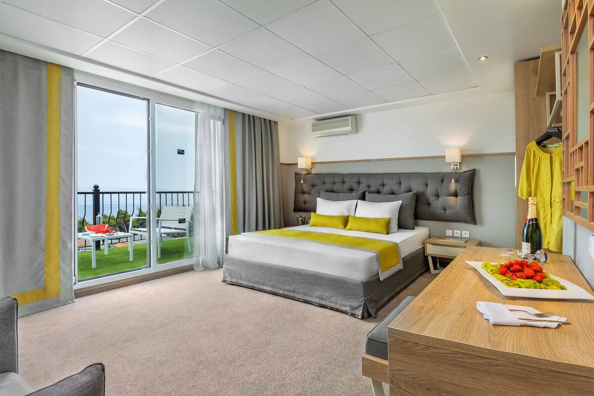 Ein Hotelzimmer mit einem großen Bett, einem Holztisch, einem Balkon mit Blick und einem Essbereich mit Obst.