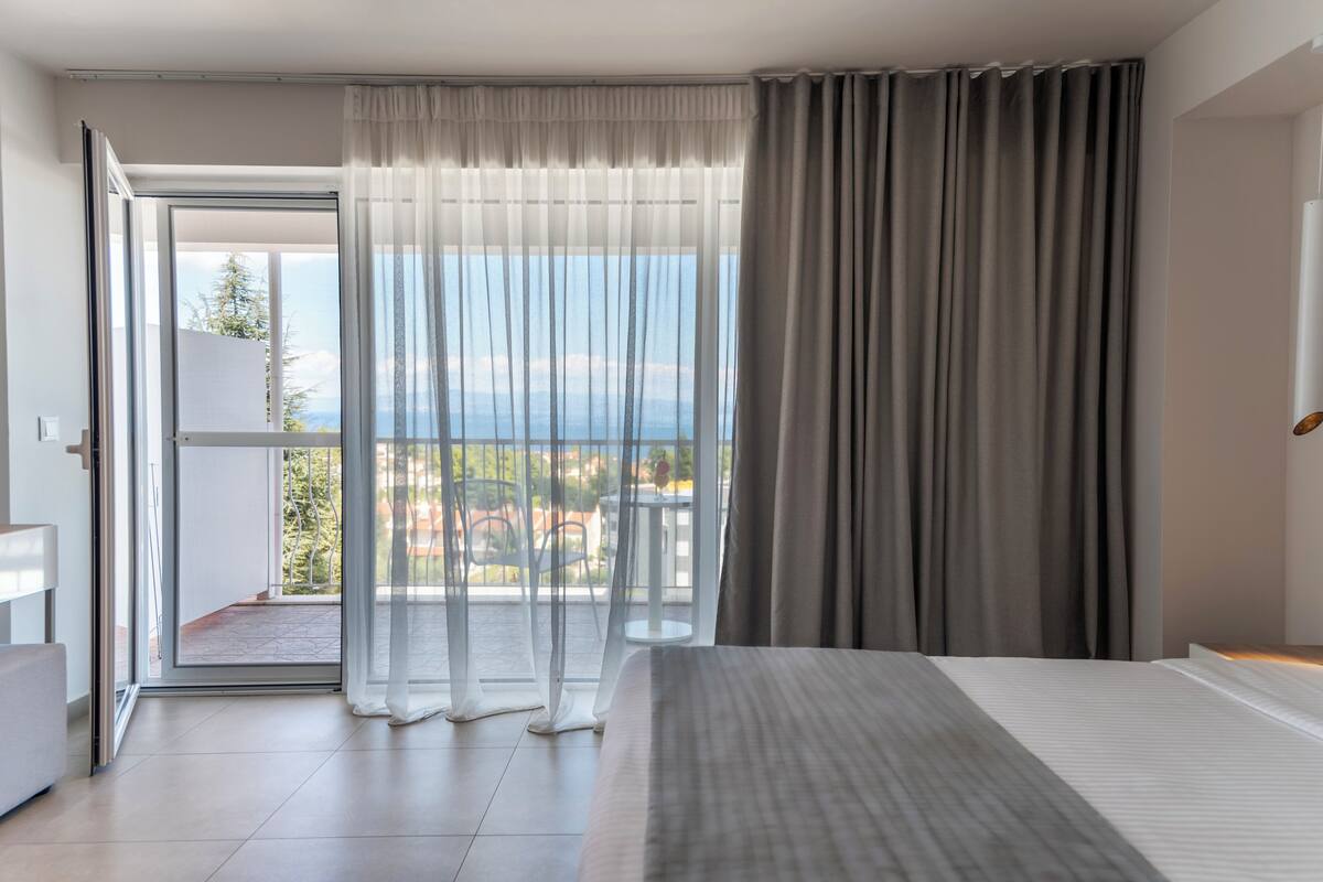 Ein modernes Hotelzimmer mit einem großen Bett, einem Balkon mit Blick auf die Stadt und einer Schiebeglastür.