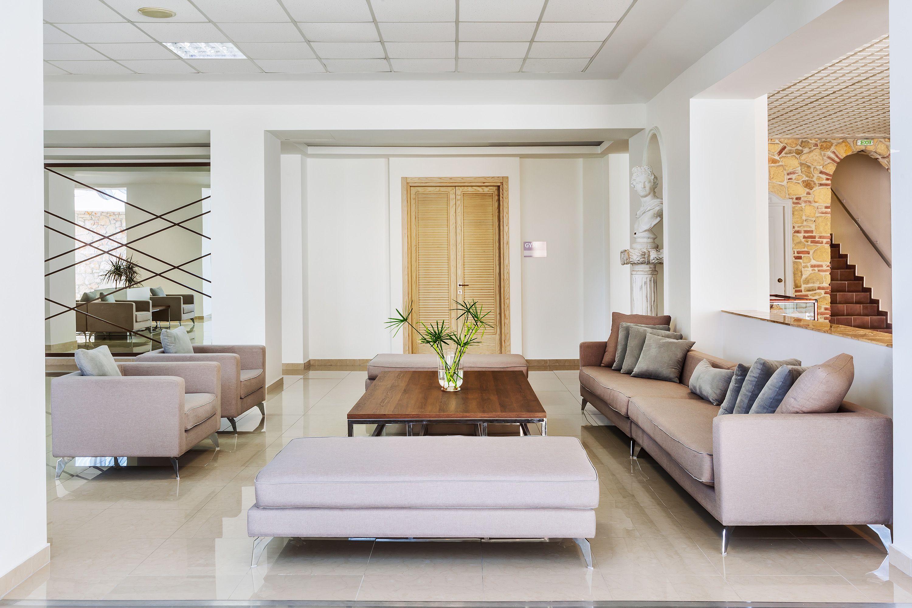 A modern living room with a wooden coffee table, beige sofas, and a glass partition.