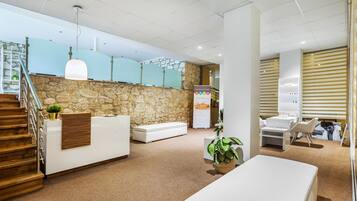 Zona de recepción con pared de piedra, escalera de madera y mostrador de recepción.