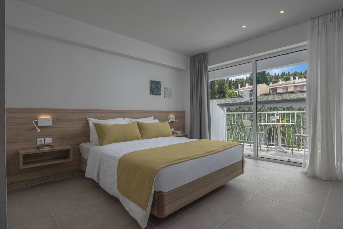Ein modernes Hotelzimmer mit einem großen Bett, einem Nachttisch, einer Wandlampe und einem Balkon mit Blick auf die Umgebung.