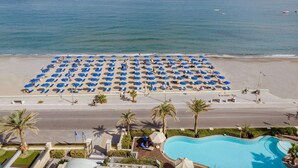 A beach with numerous blue umbrellas and a swimming pool. - Aegean Pearl (Rethymno)