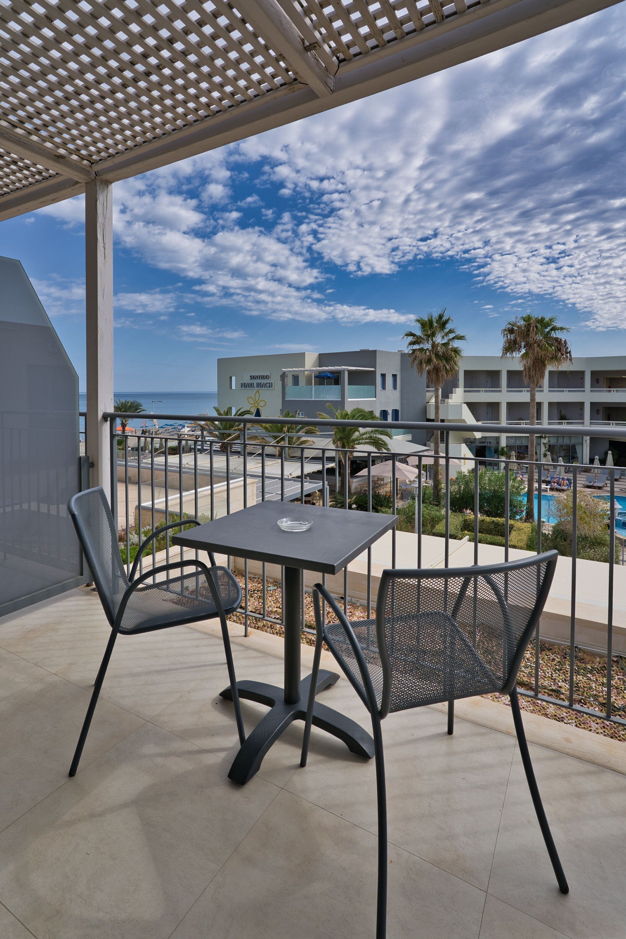 A balcony with a table and chairs, overlooking a pool and a building labeled "Sorrento Beach Club".