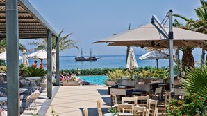 A poolside area with outdoor seating, umbrellas, and a view of the sea. - Aegean Pearl (Rethymno)