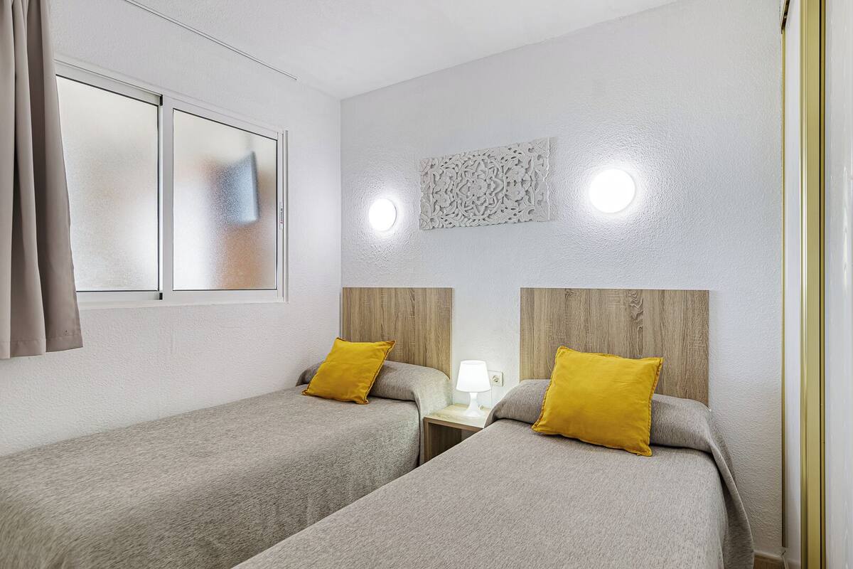 Hotellihuone, jossa on kaksi erillistä sänkyä, yöpöytä lampun kanssa ja ikkuna, jossa on verhot.