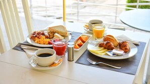 A breakfast table with plates of eggs, toast, sausages, and croissants, accompanied by cups of coffee and orange juice. - BaySide Salgados (Albufeira)