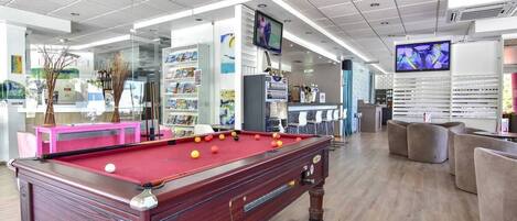 A billiards room with a pool table, seating area, and a television screen.