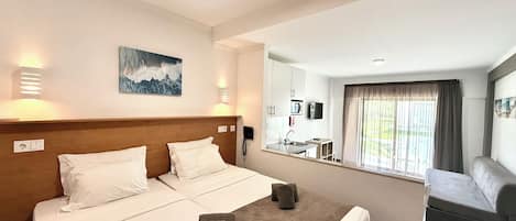A hotel room with a double bed, a small sofa, a bathroom with a sink and mirror, and a window with curtains.