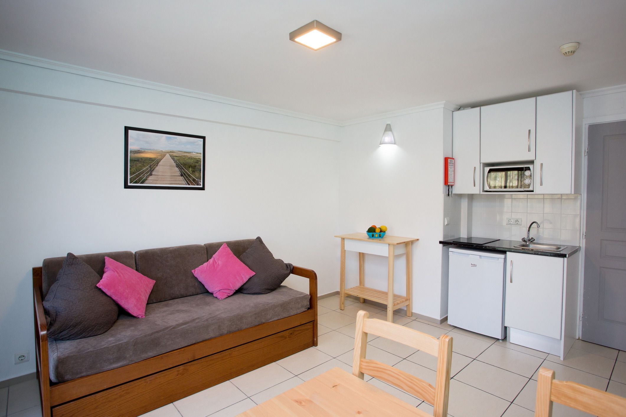Un espacio habitable compacto con sofá, una mesita, kitchenette y un cuadro en la pared.