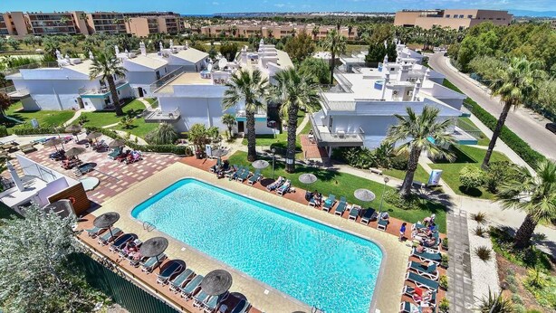 A resort with a swimming pool surrounded by lounge chairs and palm trees. - BaySide Salgados (Albufeira)