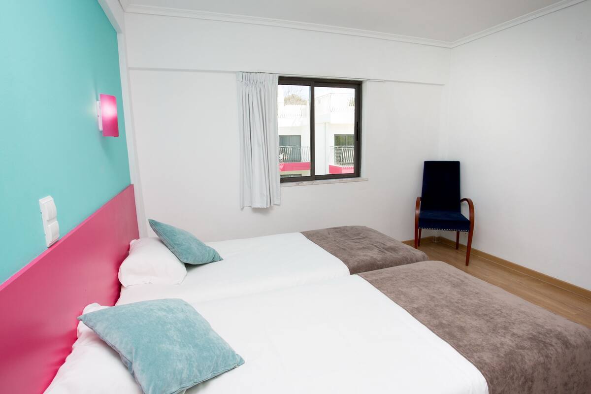 A bedroom with a bed, a chair, a window, and a view of a balcony.