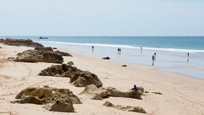 A beach with large rocks and people walking along the shore. - BaySide Salgados (Albufeira)