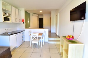 Una cocina moderna con armarios blancos, un microondas y un lavabo. Hay un comedor con una mesa y sillas. Un televisor de pantalla plana está montado en la pared.