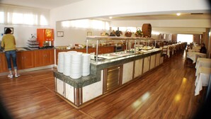 A buffet area with a counter, stacked plates, and various food items. - Hotel Kristal (Torremolinos)