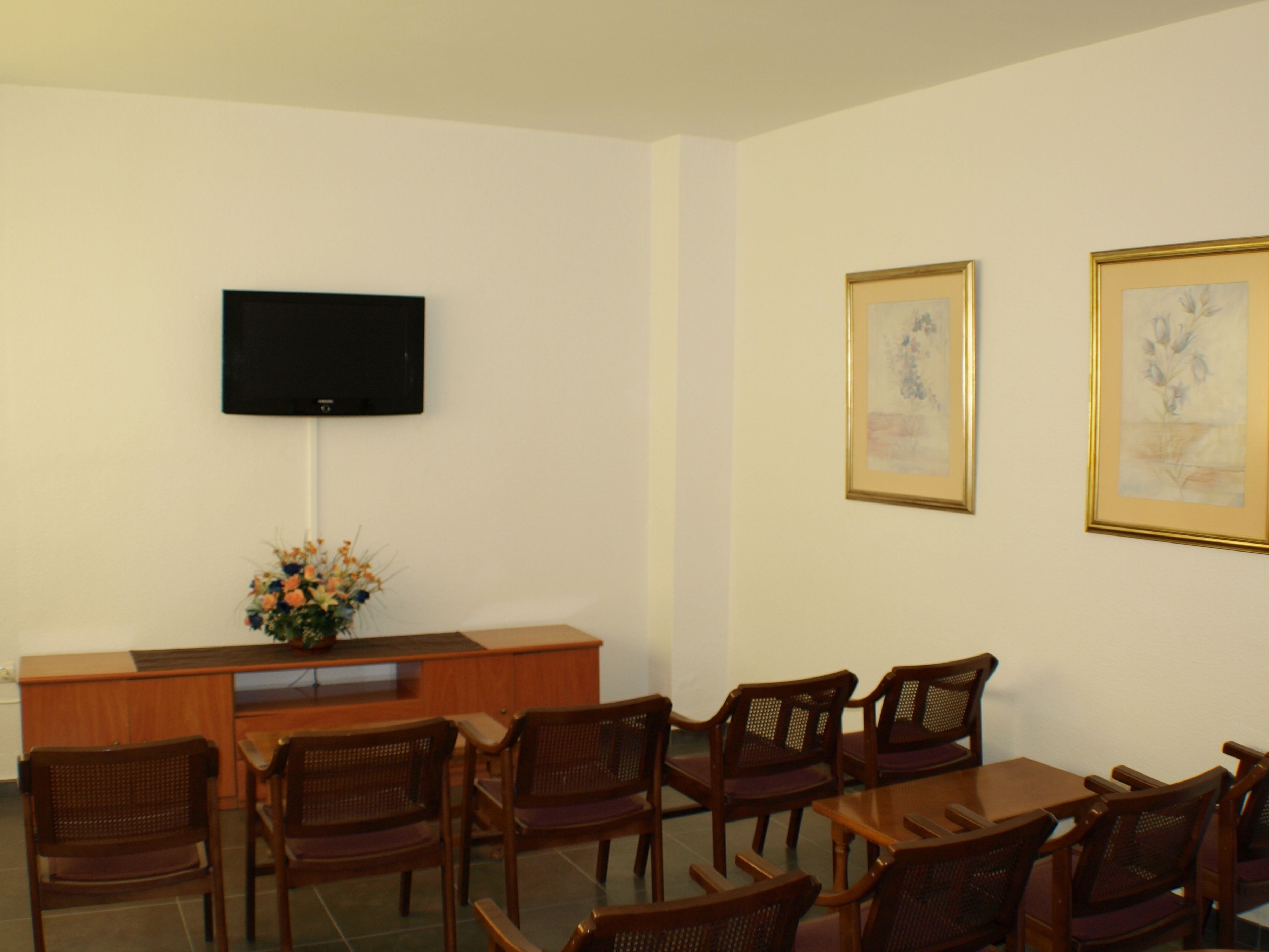 A conference room with a wooden table and chairs, a flat-screen TV mounted on the wall, and two framed artworks on the wall.