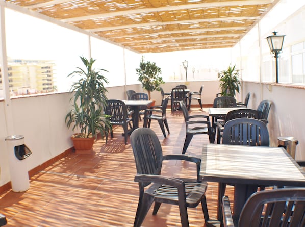 Une terrasse extérieure avec des tables et des chaises, des plantes en pot et une vue sur les bâtiments en arrière-plan.