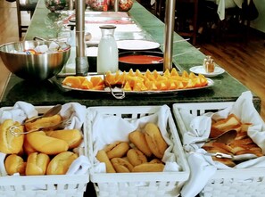 Une table de buffet proposant divers aliments, notamment des tranches d’orange, du pain et un bol de condiments.