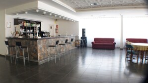 A modern bar area with a stone counter, bar stools, and a red sofa in a spacious room with a tiled floor and a large window. - Hotel Kristal (Torremolinos)