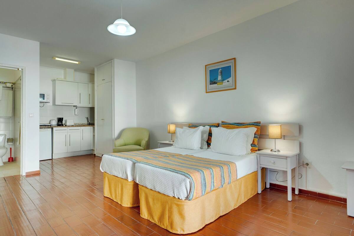 Una camera d'albergo con un letto, comodini, una sedia, una scrivania e angolo cottura.