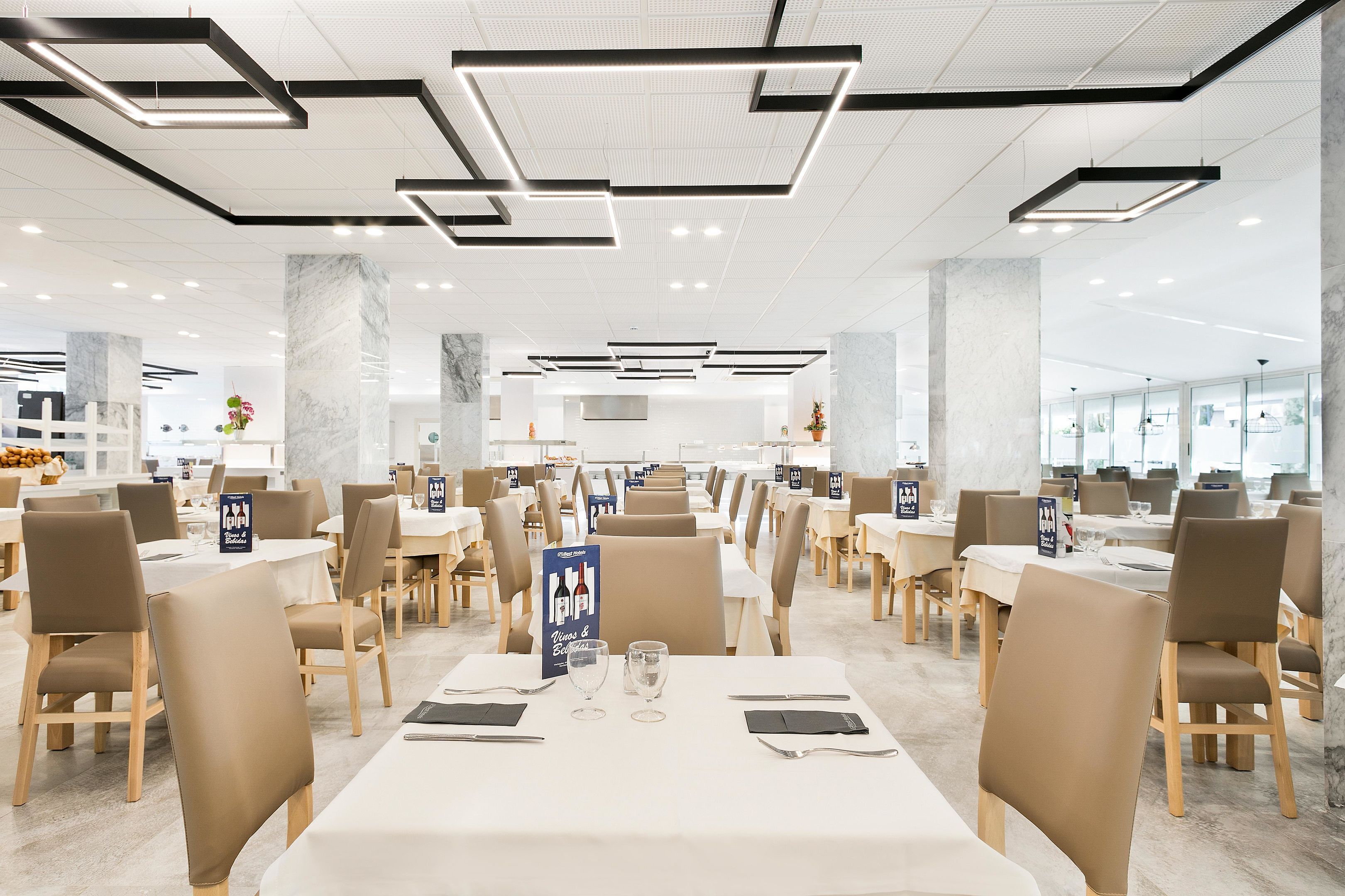 A spacious restaurant with multiple dining tables and chairs, featuring a modern ceiling design and marble columns.