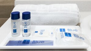 A bathroom with a white towel, two bottles of Blue shampoo and gel, and a tray with Blue shower gel and a bar of soap. - Hotel Best Da Vinci  (Salou)