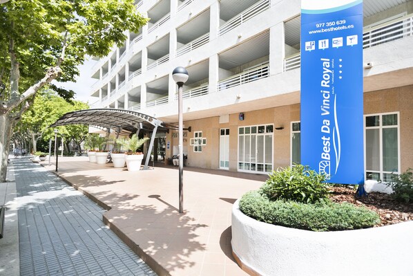 L’entrée d’un hôtel, avec une grande enseigne bleue, une allée couverte et un espace paysager.