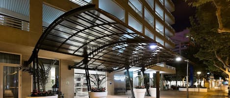 A hotel entrance with a covered walkway, large potted plants, and a sign reading "Best Da Vinci".