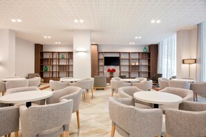 Een moderne eetruimte met ronde tafels en grijze gestoffeerde stoelen, houten boekenkasten en een grote flatscreen-televisie.