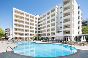 A multi-story hotel with a swimming pool, outdoor seating, and a clear blue sky.