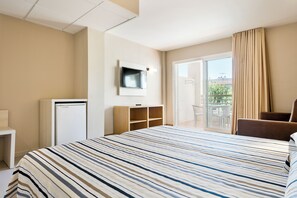 Een hotelkamer met een bed, een aan de muur bevestigde televisie, een klein bureau, een kledingkast en een balkon met een stoel.