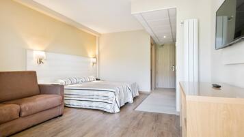 Une chambre d’hôtel moderne, dotée d’un canapé, d’un lit avec une literie à rayures, d’un bureau en bois et d’un téléviseur à écran plat fixé au mur.