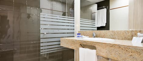 A modern bathroom with a glass shower enclosure, a granite countertop sink, and a towel rack.