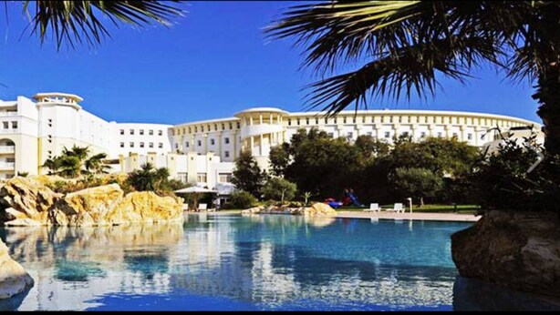 A large hotel with a pool, surrounded by palm trees and rocks. - Medina Belisaire &Thalasso (Hammamet)