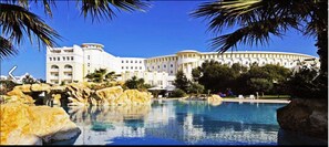A large hotel with a pool, surrounded by palm trees and rocks. - Medina Belisaire &Thalasso (Hammamet)