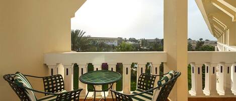 Un balcon avec une table et des chaises, une vue sur les bâtiments et les arbres, et une balustrade blanche.
