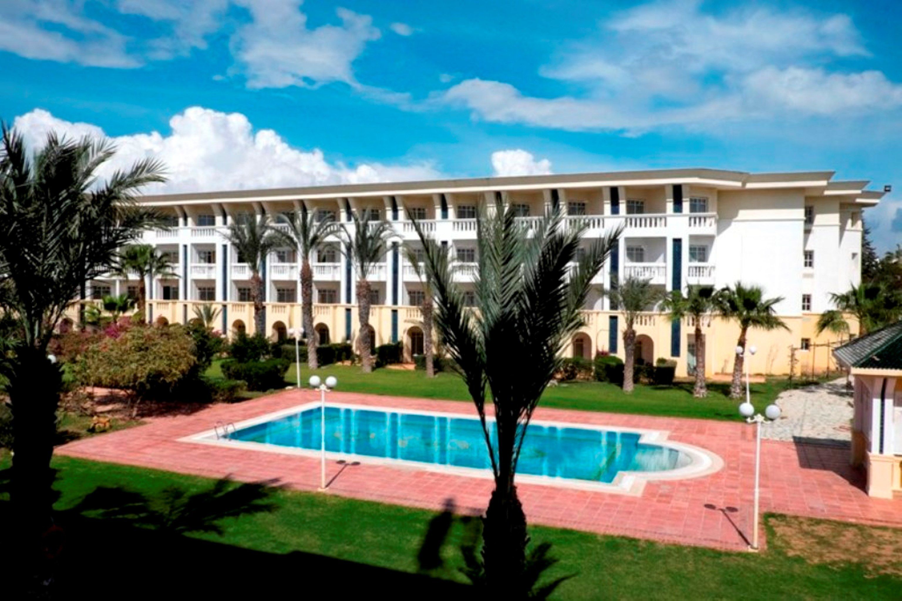 Un hotel con piscina, palmeras y cielo azul despejado.
