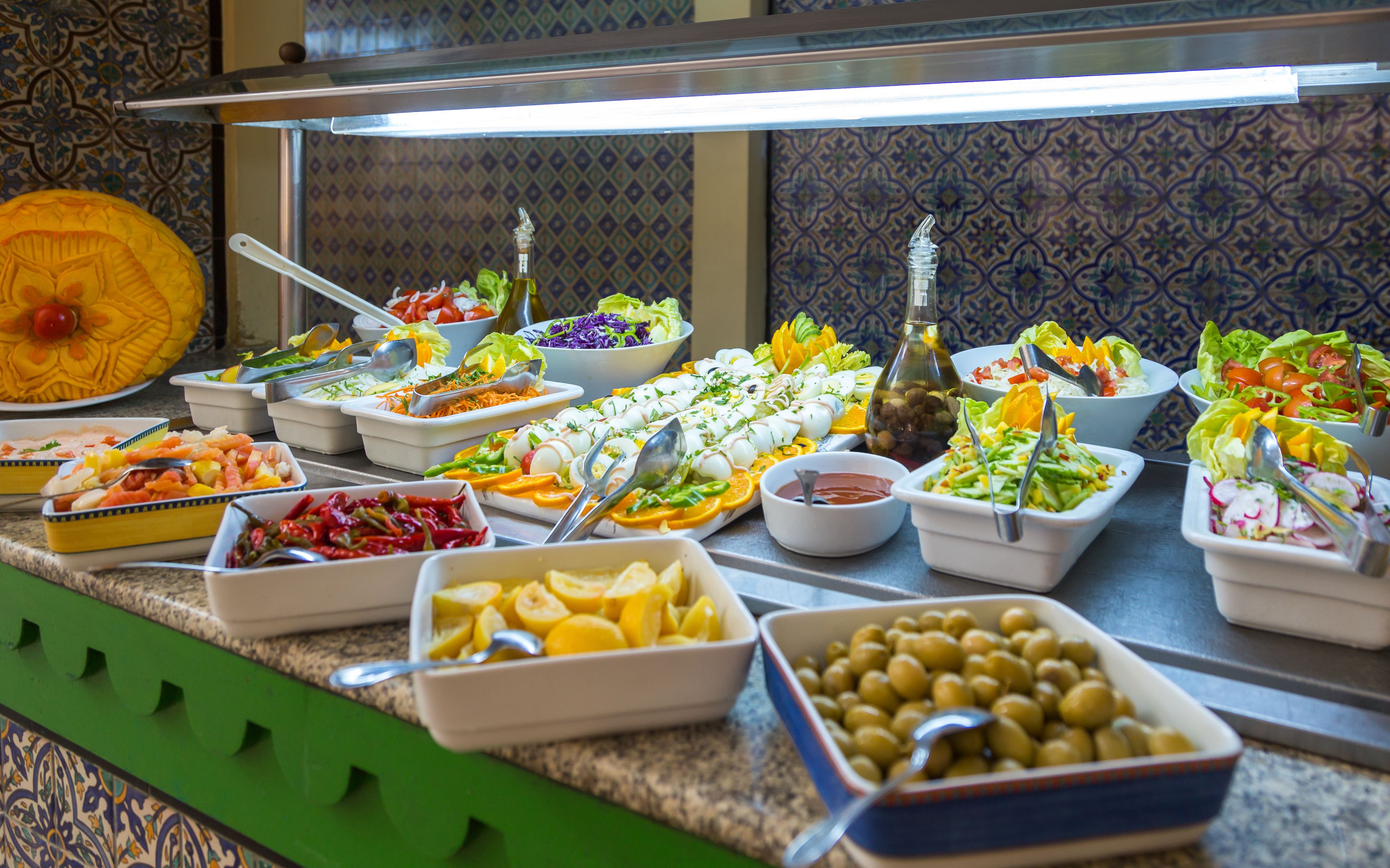 Un bufé con diversos platos, incluidas ensaladas, frutas y verduras.
