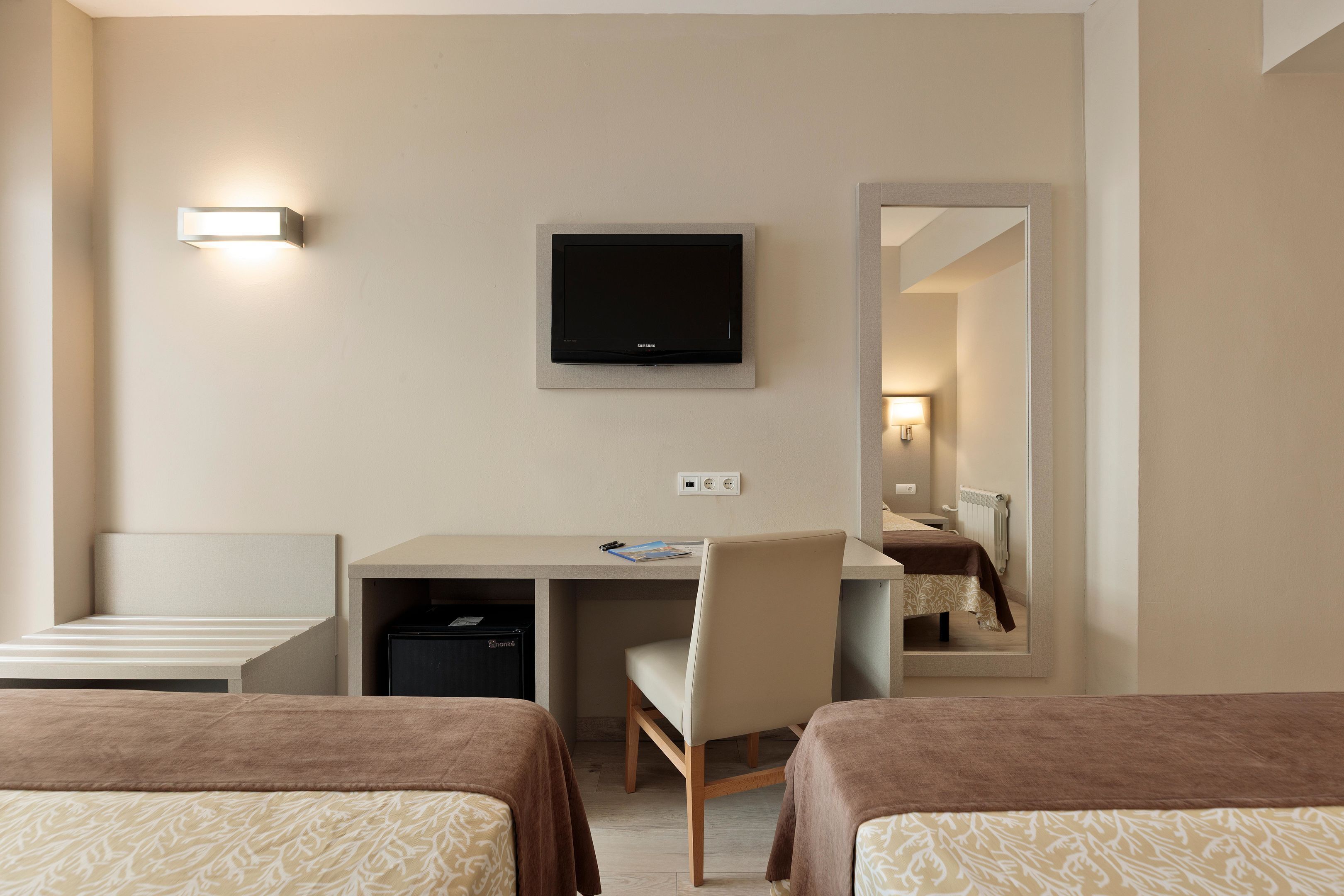 Una habitación de hotel con dos camas, un escritorio, una silla, un televisor y un espejo.